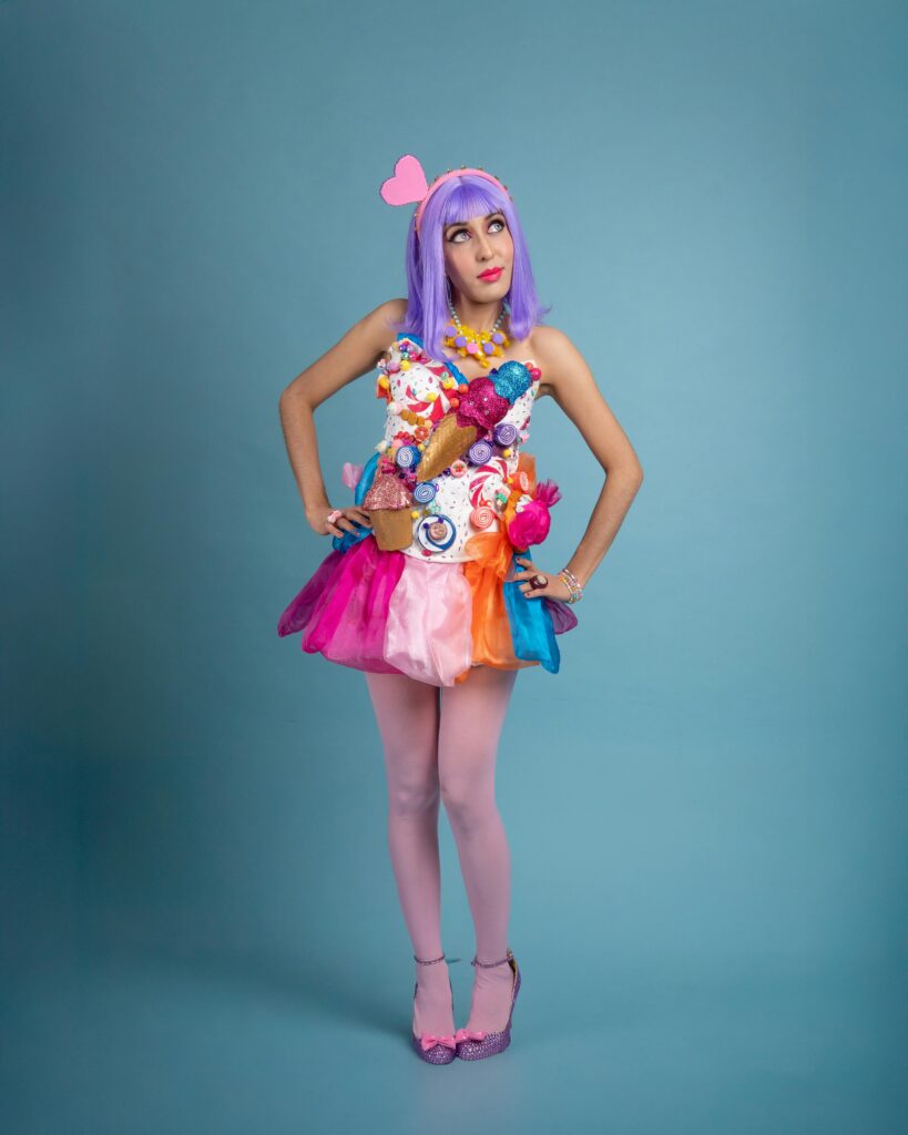 Vibrant cosplay portrait of a young woman in candy-inspired attire against a blue backdrop.